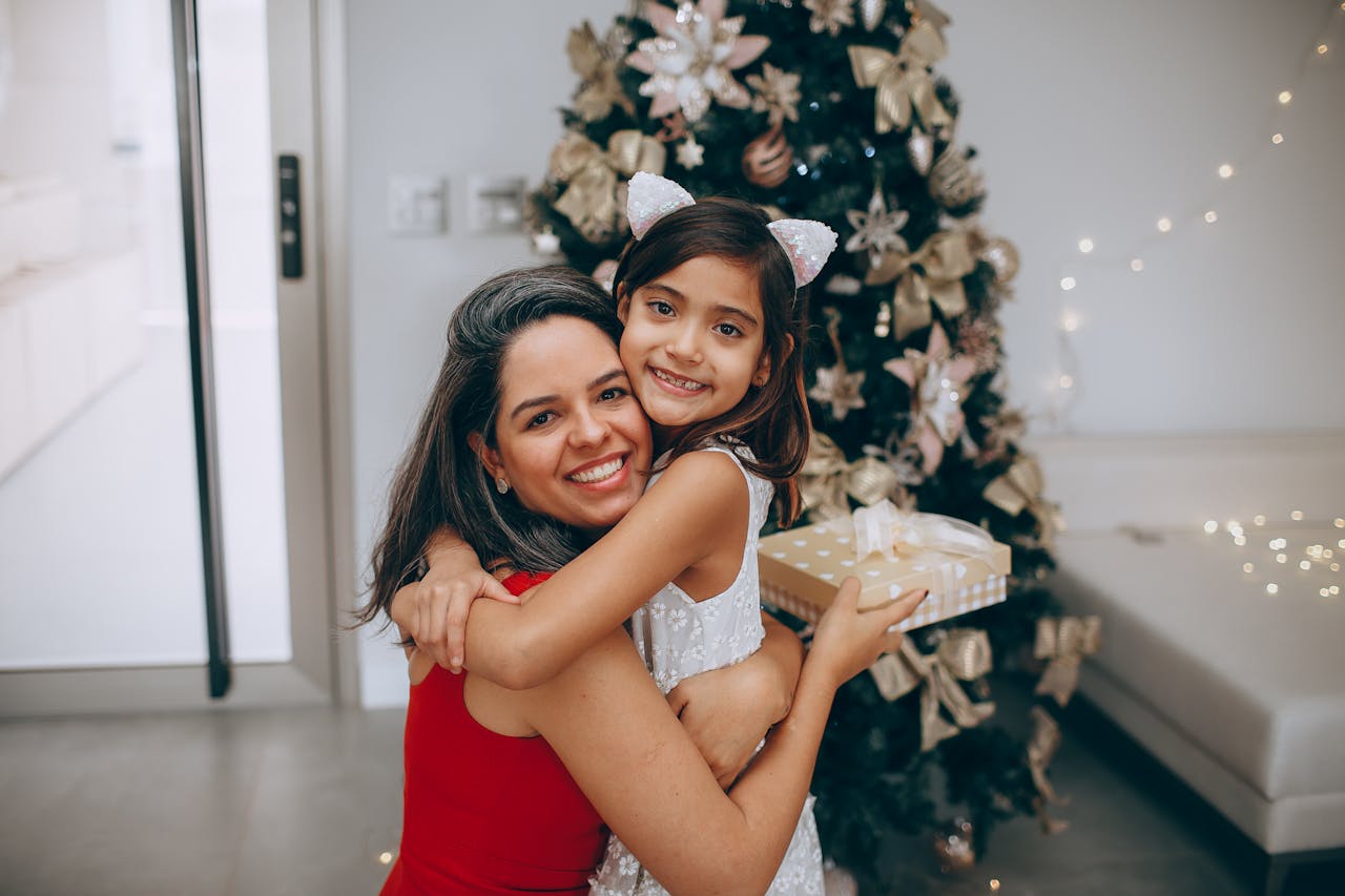 Mother hugs her daughter beside a decorated Christmas tree, reflecting family traditions after divorce.